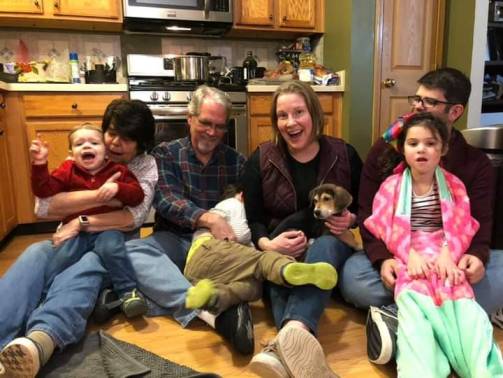 Mom, dad, my wife Becca and me sit on the kitchen floor. Mom holds my son, Gavin. Dad attempts to wrangle my nephew Gino. Becca is holding the puppy Apollo and I'm holding my niece Evie